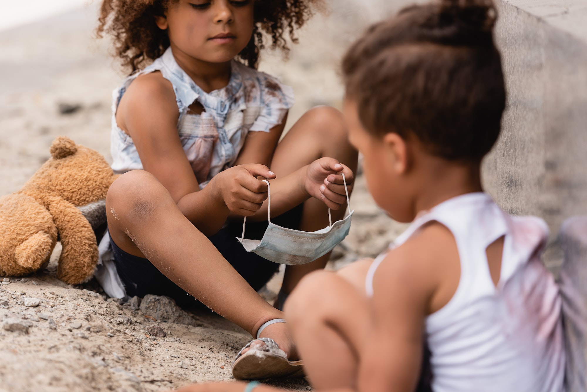 selective-focus-of-curly-african-american-child-holding-dirty-medical-mask-near-poor-brother-sitting.jpg